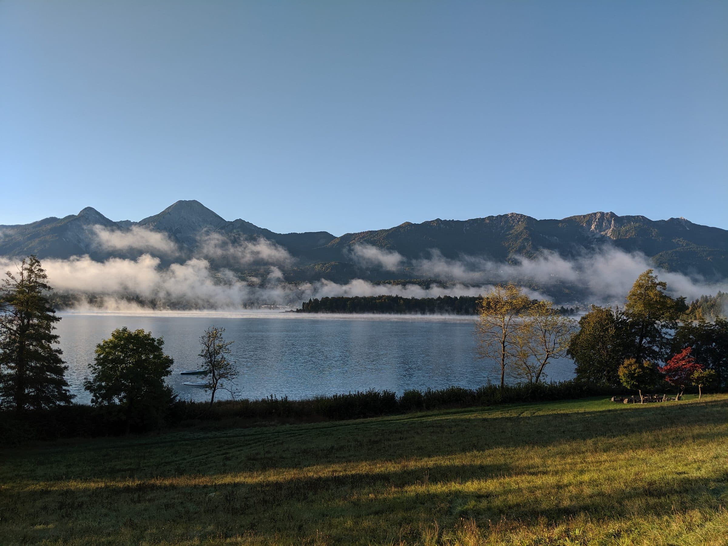 Morgennebel über einem stillen Kärntner See mit Bergen im Hintergrund